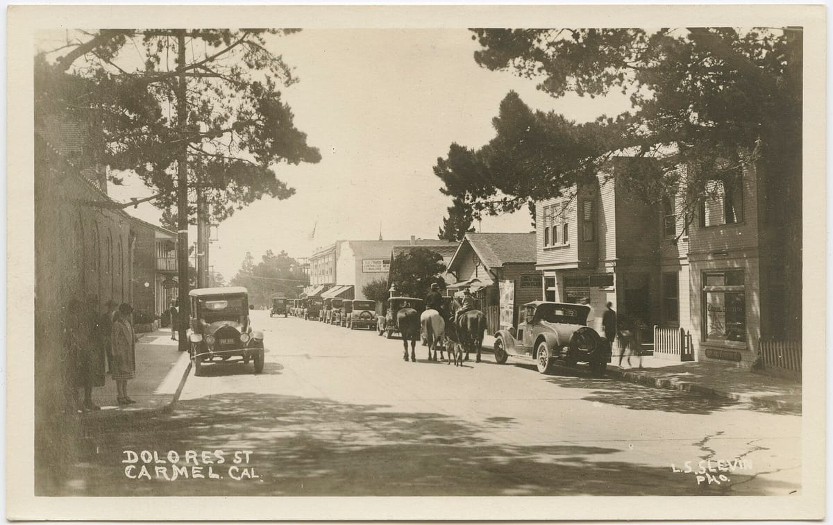 Dolores Street in an early postcard view, with cars parked under pines