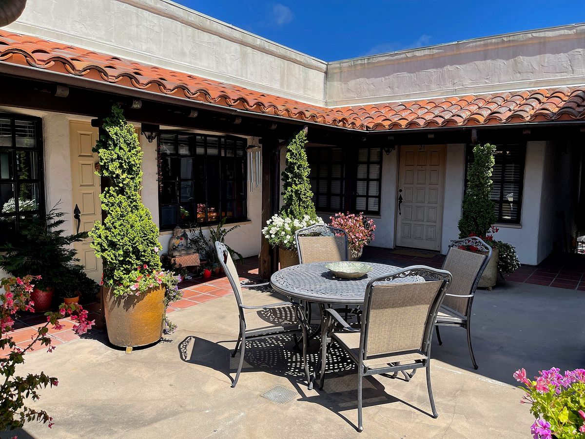 A tile-roofed courtyard with flower pots and chairs, off a Carmel street